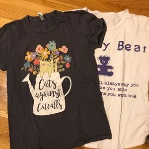 Two small graphic t-shirts that say “Cats Against Catcalls” and “Browny Bear”